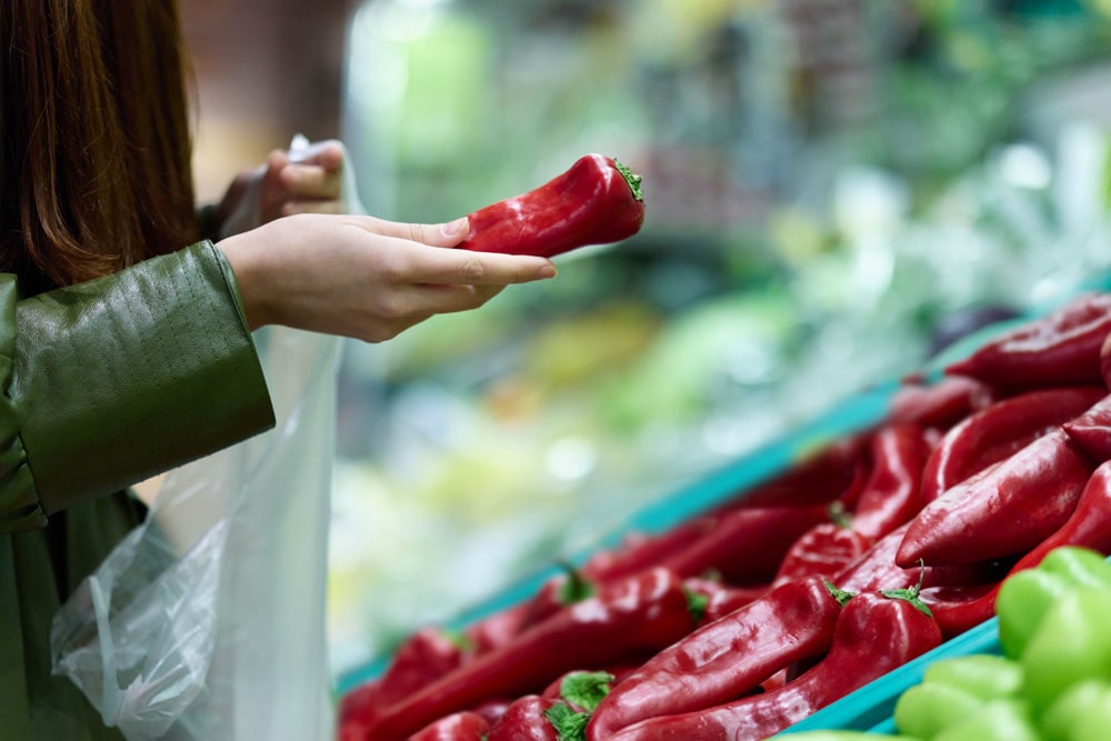 Frau hält im Supermarkt eine Paprika in der Hand